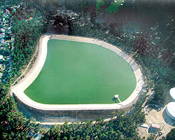 Aerial view of a large, shield-shaped water reservoir surrounded by trees.
