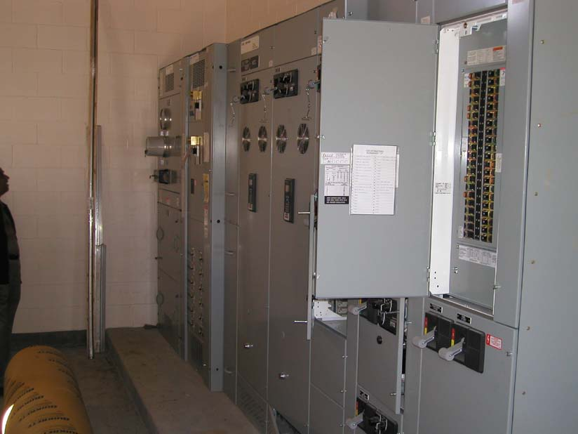 A row of gray industrial electrical panels with gauges, switches, and wiring, possibly in an electrical room.
