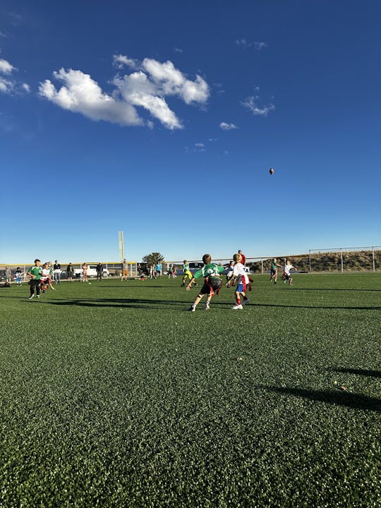Children playing soccer on a sunny day with a clear blue sky and a few clouds.