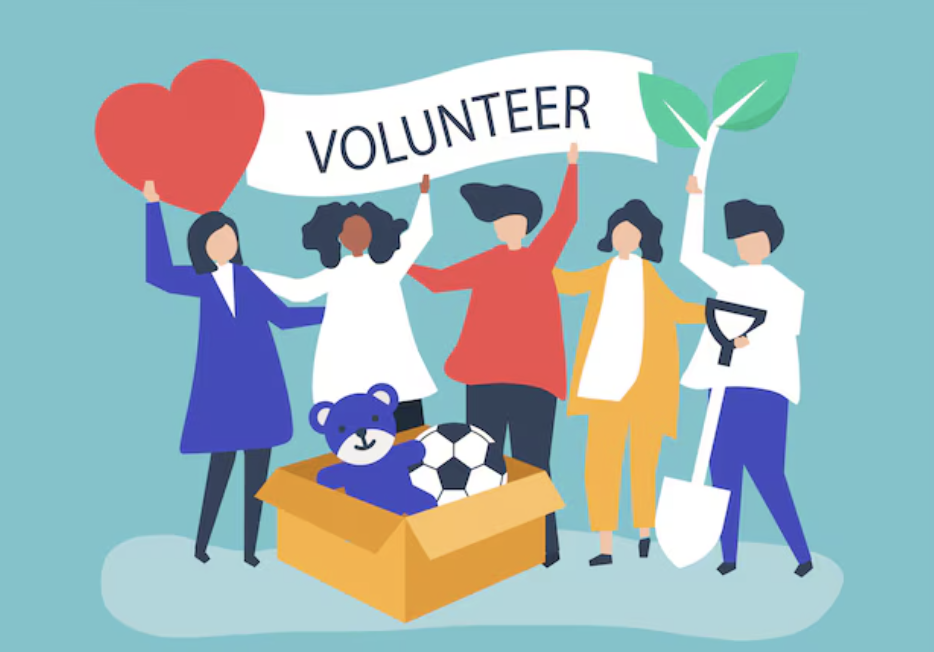 Five people holding a "Volunteer" banner, a heart, and a plant, standing by a box with a teddy bear and a soccer ball.