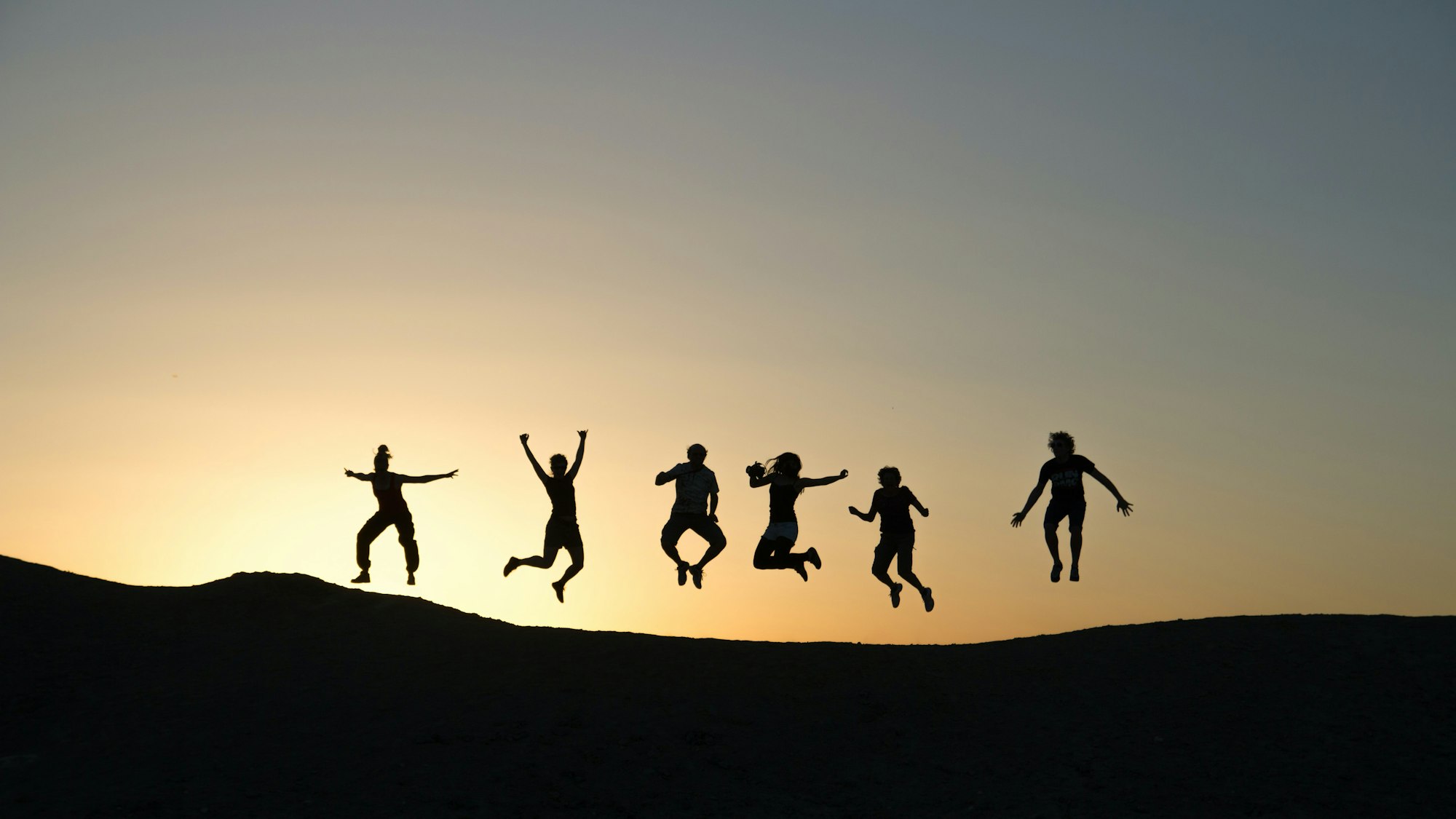 Silhouettes of seven people leaping joyfully against a sunset sky.