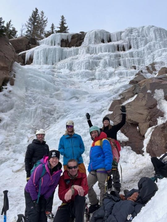 Group of people in winter gear posing in front of a frozen waterfall.