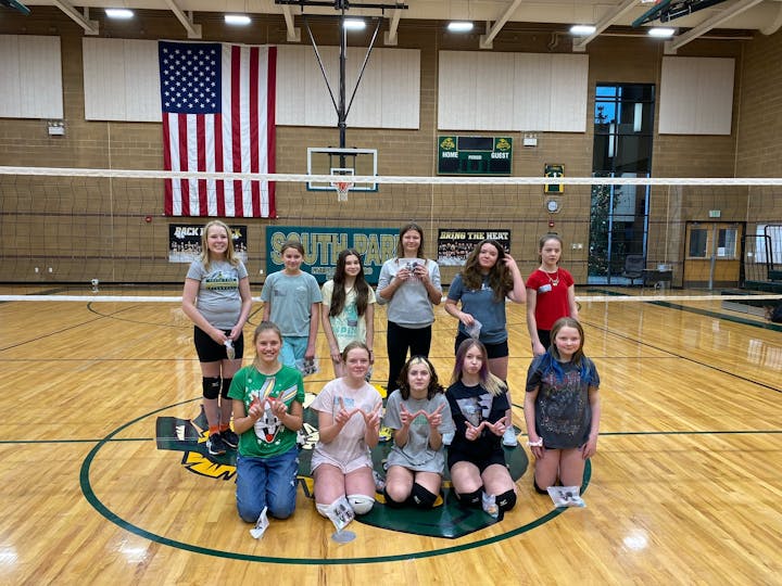 Group of young volleyball players posing in a gymnasium with an American flag in the background.