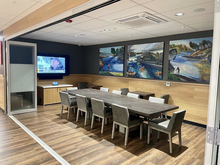 Meeting room with a long table, chairs, a TV screen, and colorful paintings on the wall.