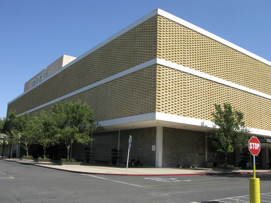 The image shows a modern building with a patterned exterior, likely a retail store, surrounded by greenery and a stop sign.