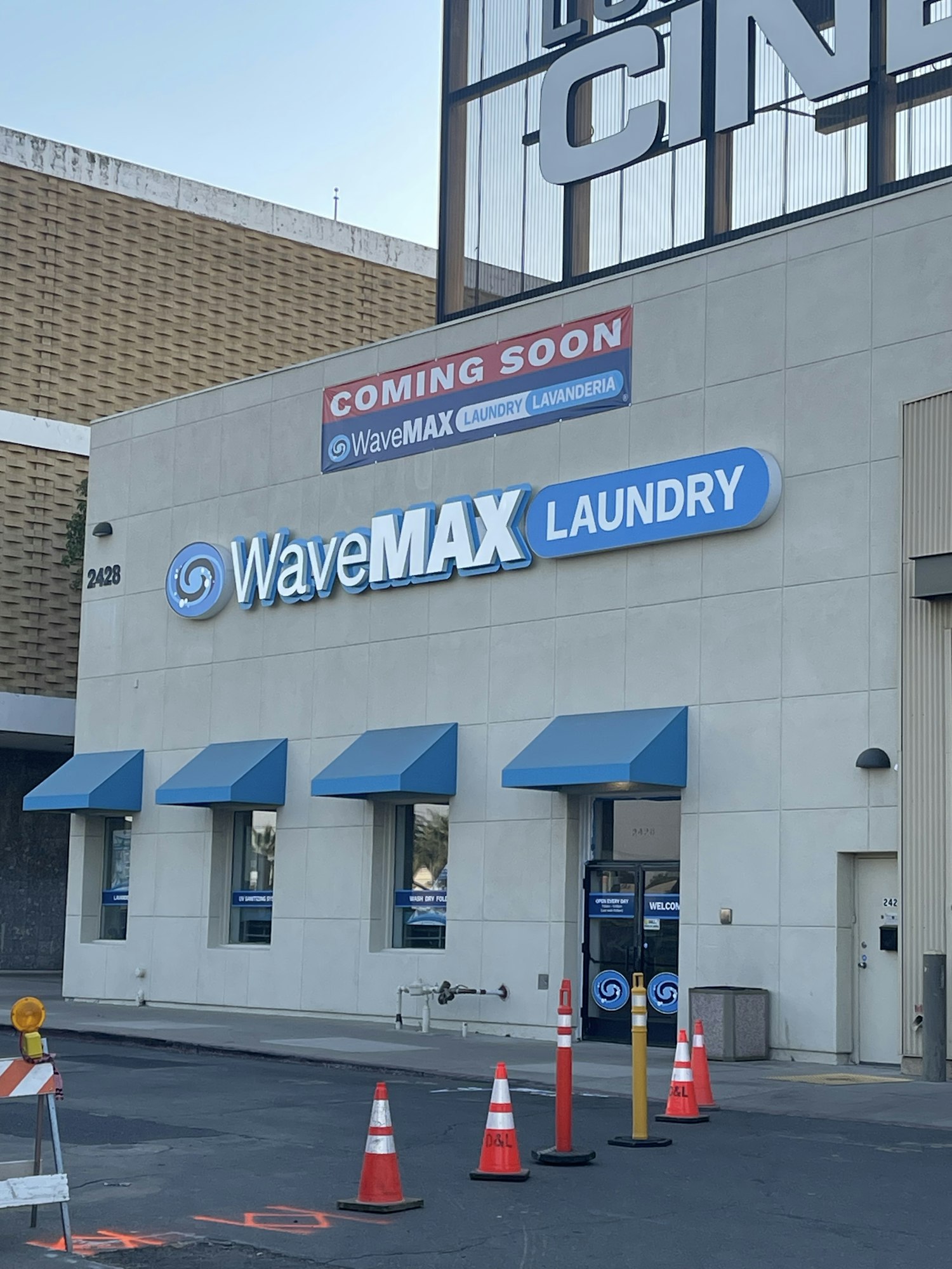 Building with "WaveMAX Laundry" sign, blue awnings, and traffic cones. "Coming Soon" banner visible.