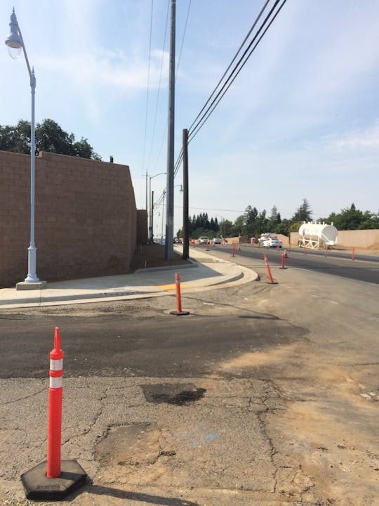 The image shows a street under construction with traffic cones, utility poles, and a concrete mixer in the background.