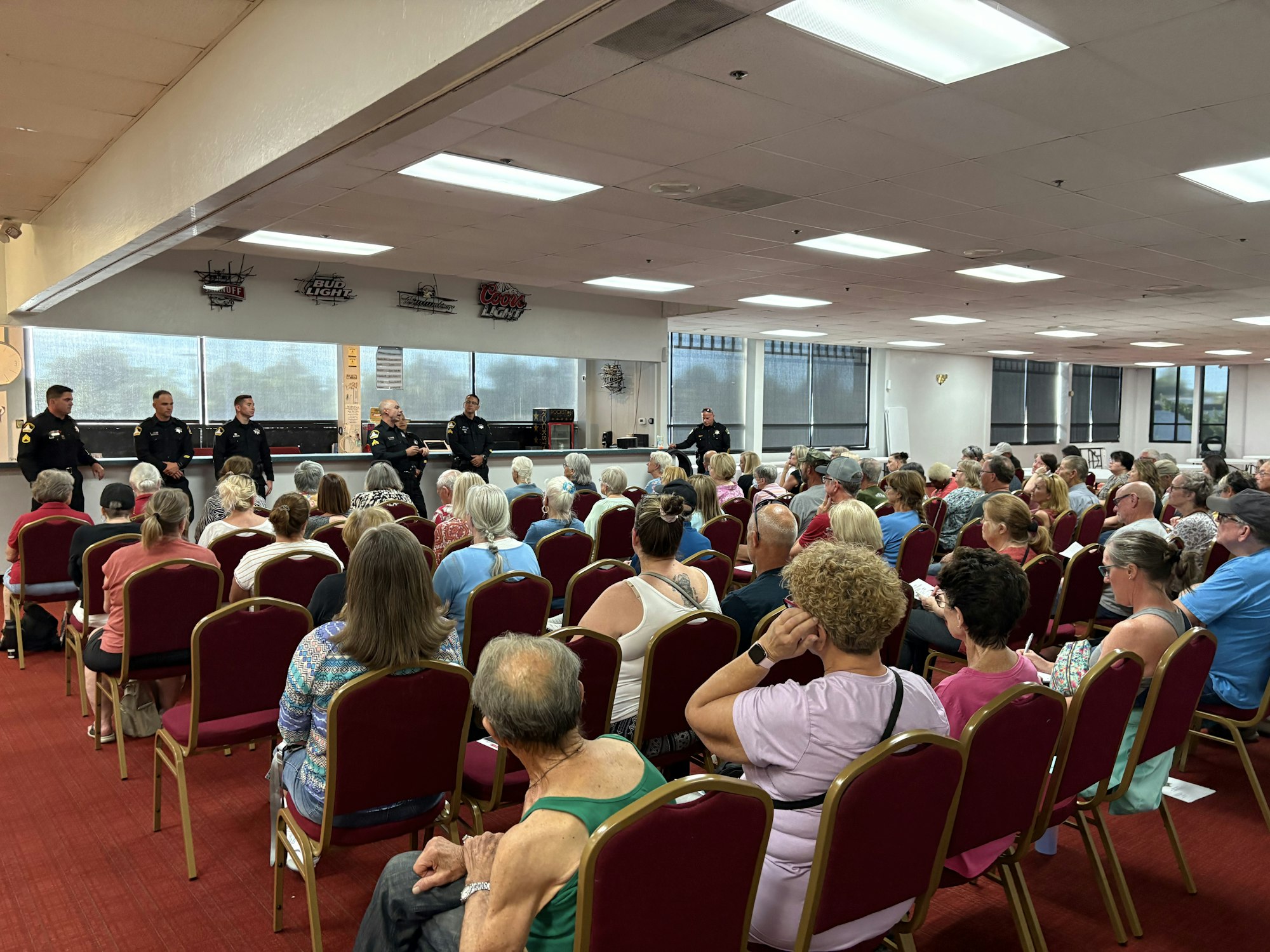 A public meeting with police officers speaking to a large audience seated in a hall.