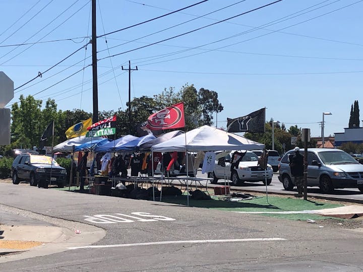 A street scene featuring tents, various flags, and people, likely at a community event or gathering.