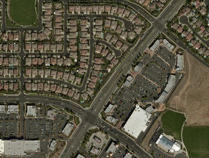 An aerial view of a suburban area featuring residential neighborhoods, a retail complex, and surrounding roads.