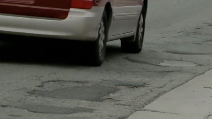Rear of a red car near a pothole on an asphalt road.