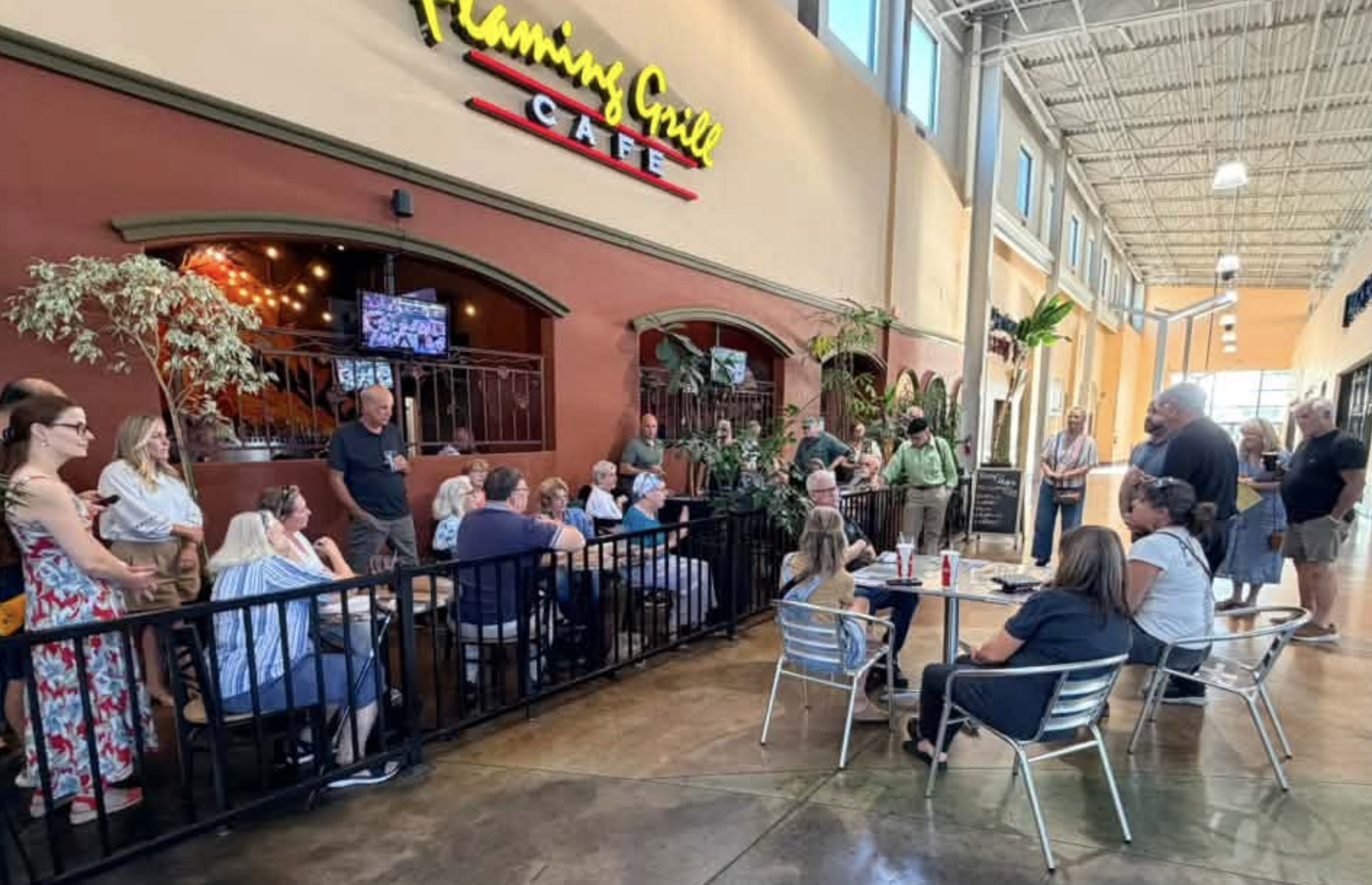 A group of people is gathered at Flaming Grill Café, some seated at tables, while others stand nearby, engaged in conversation.
