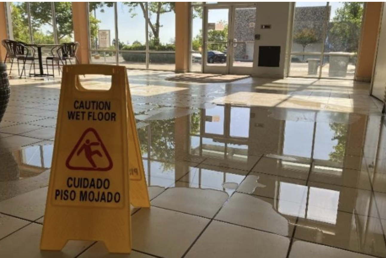 Wet floor caution sign on a tiled floor with puddles and reflections.