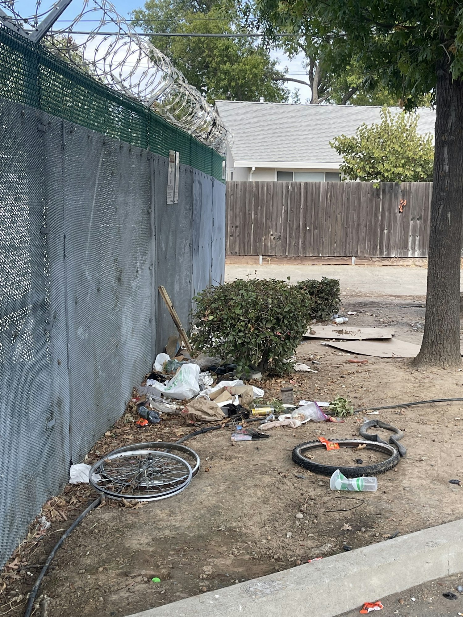 A fenced area with a barbed wire top, discarded bike wheels, trash, and debris on the ground.