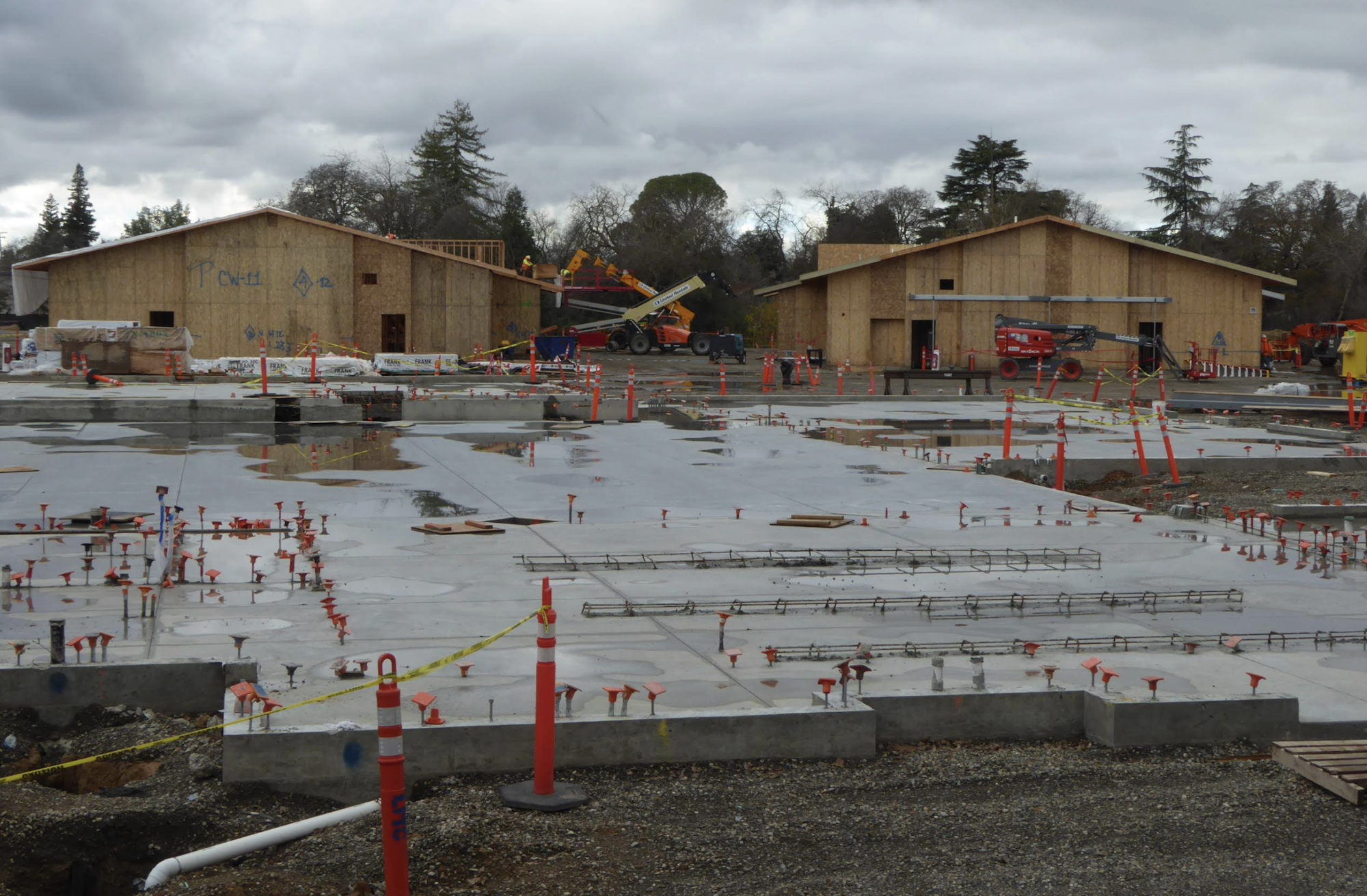 A construction site with concrete foundation work and two wooden frame buildings.