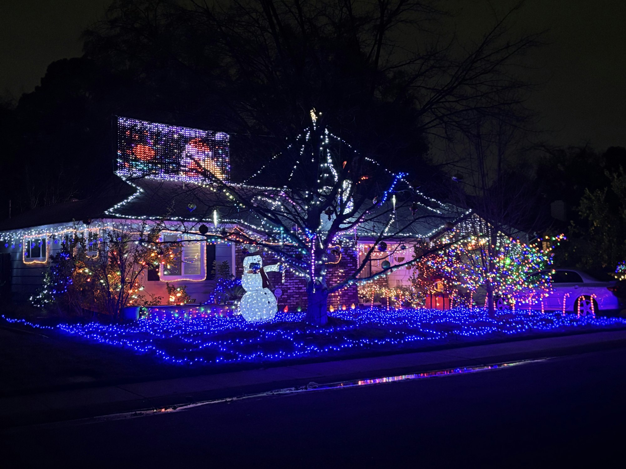 House decorated with Christmas lights, including a lit snowman and colorful trees.
