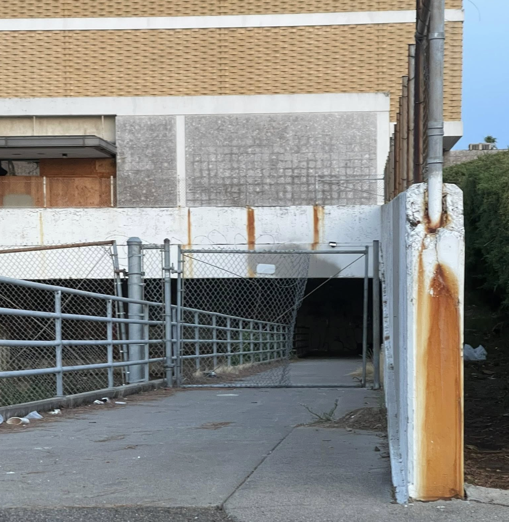 An opening used by homeless people, in the chain link fence leading underneath the boarded-up Macy's building at Country Club Plaza