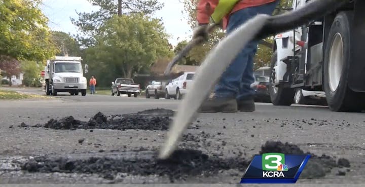 Road repair work with a person using a tool, vehicles, and asphalt.