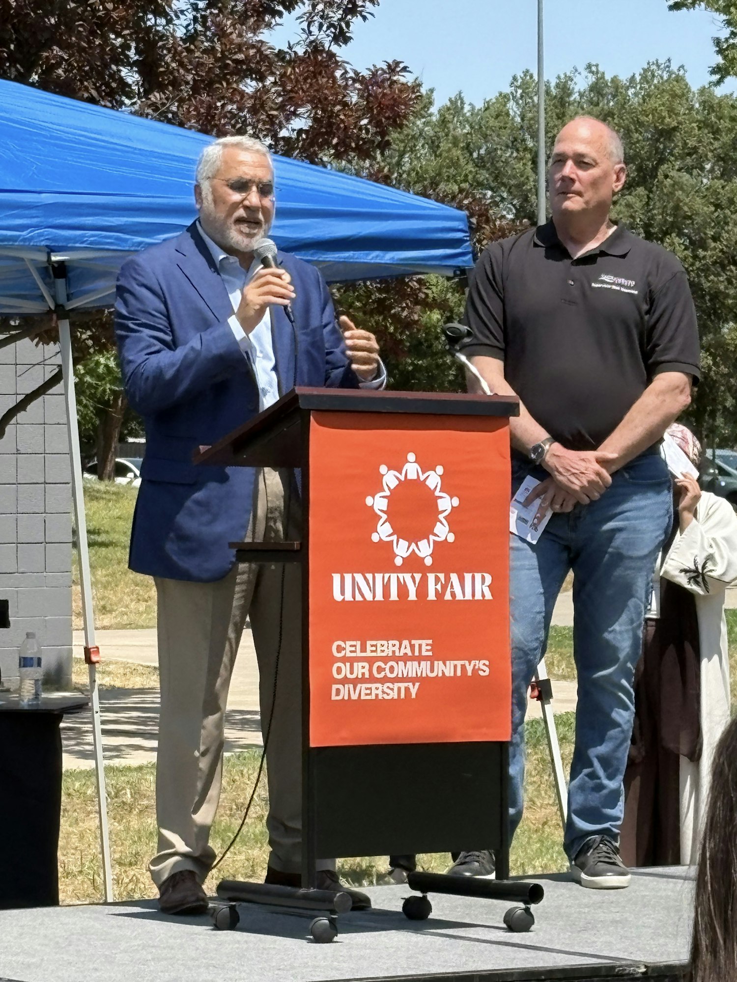 Two men stand at a podium labeled "Unity Fair" with a message to celebrate community diversity.