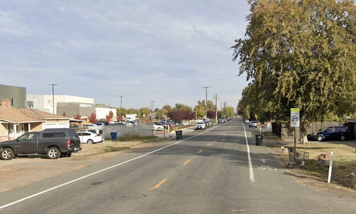 Bell Street at Carlsbad, a pedestrian vs. car site. The photo shows the street lacks sidewalks needed for access to Dyer-Kelly school and that trash bins block the marked bike route.