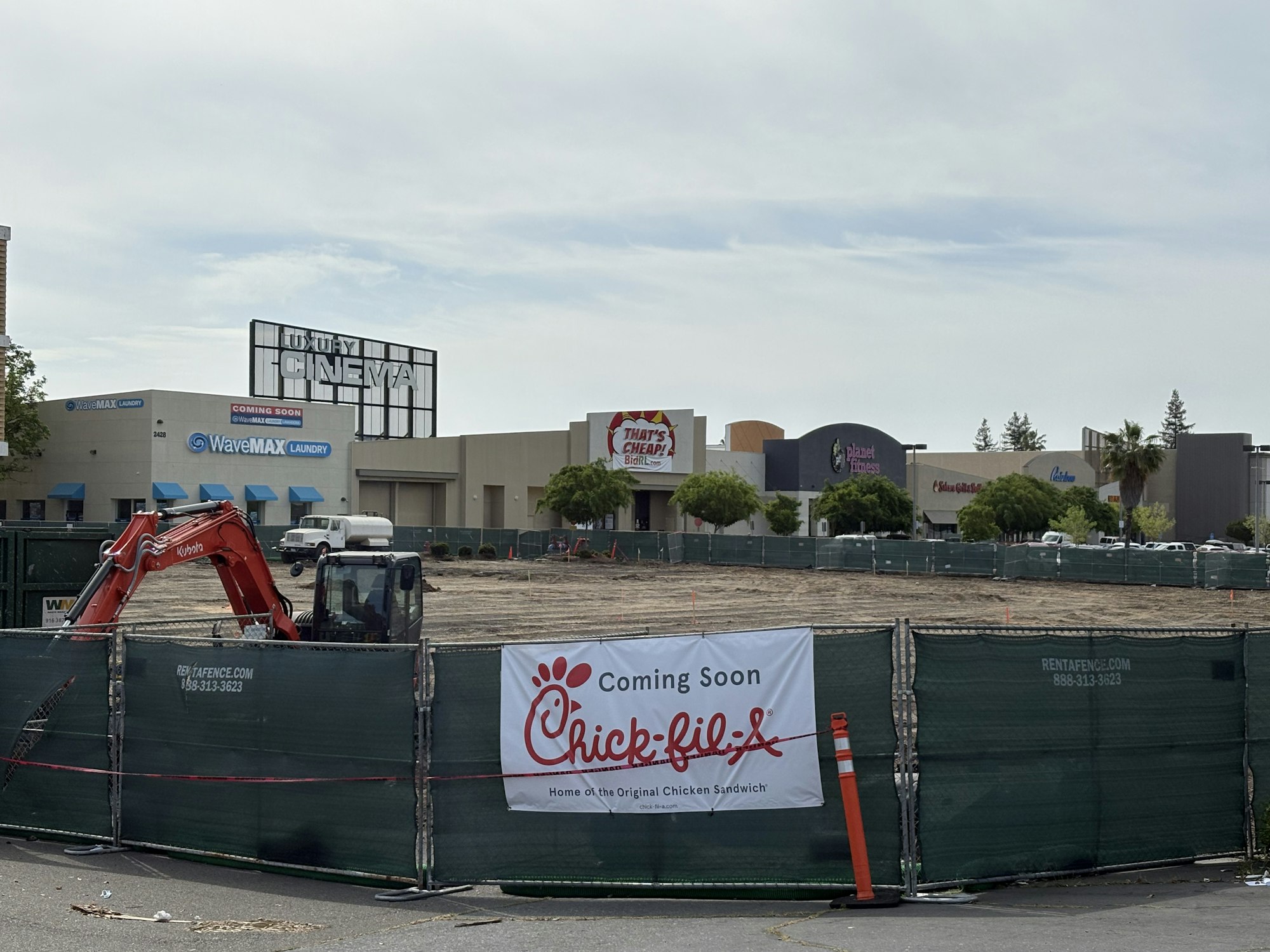 Construction site for a Chick-fil-A, with signs for a cinema, laundry, and gym in the background.