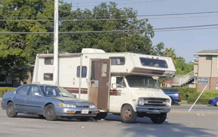 An old RV with an open door next to a sedan at a roadside.