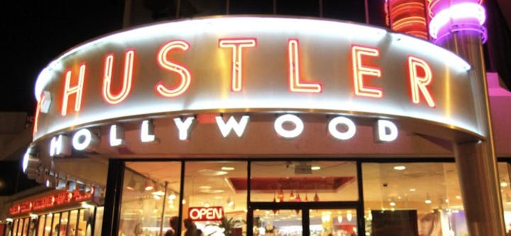 The image shows a brightly lit sign for "HUSTLER HOLLYWOOD," indicating it's an adult-themed store in Hollywood.