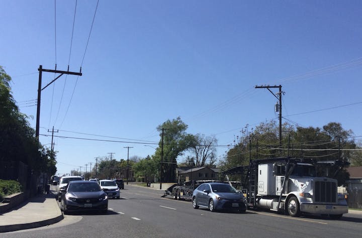 A street scene with cars, a semi-truck, power lines, and a clear sky.