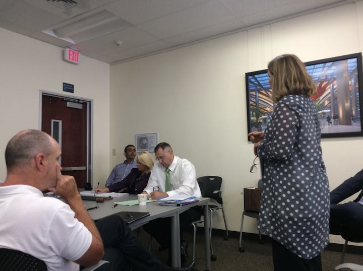 A group of people is engaged in a meeting, with one person speaking while others take notes.