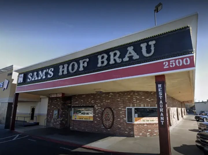 Exterior of "Sam's Hof Brau" restaurant with parking lot, signage, and brick facade.