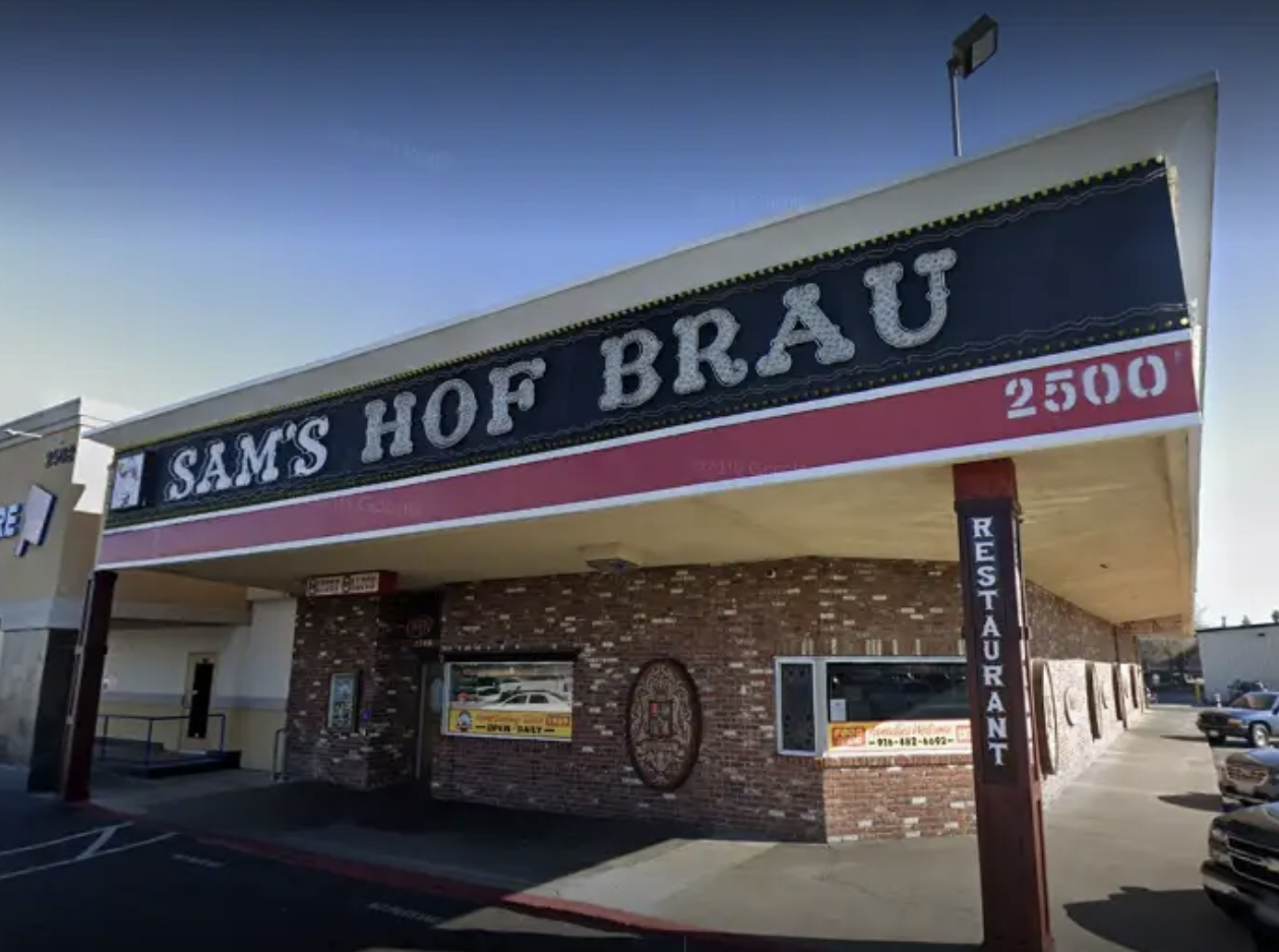 Exterior of "Sam's Hof Brau" restaurant with parking lot, signage, and brick facade.