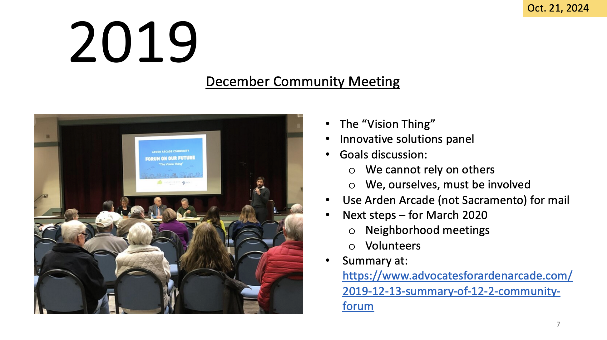 A community meeting presentation slide with attendees listening to a speaker.