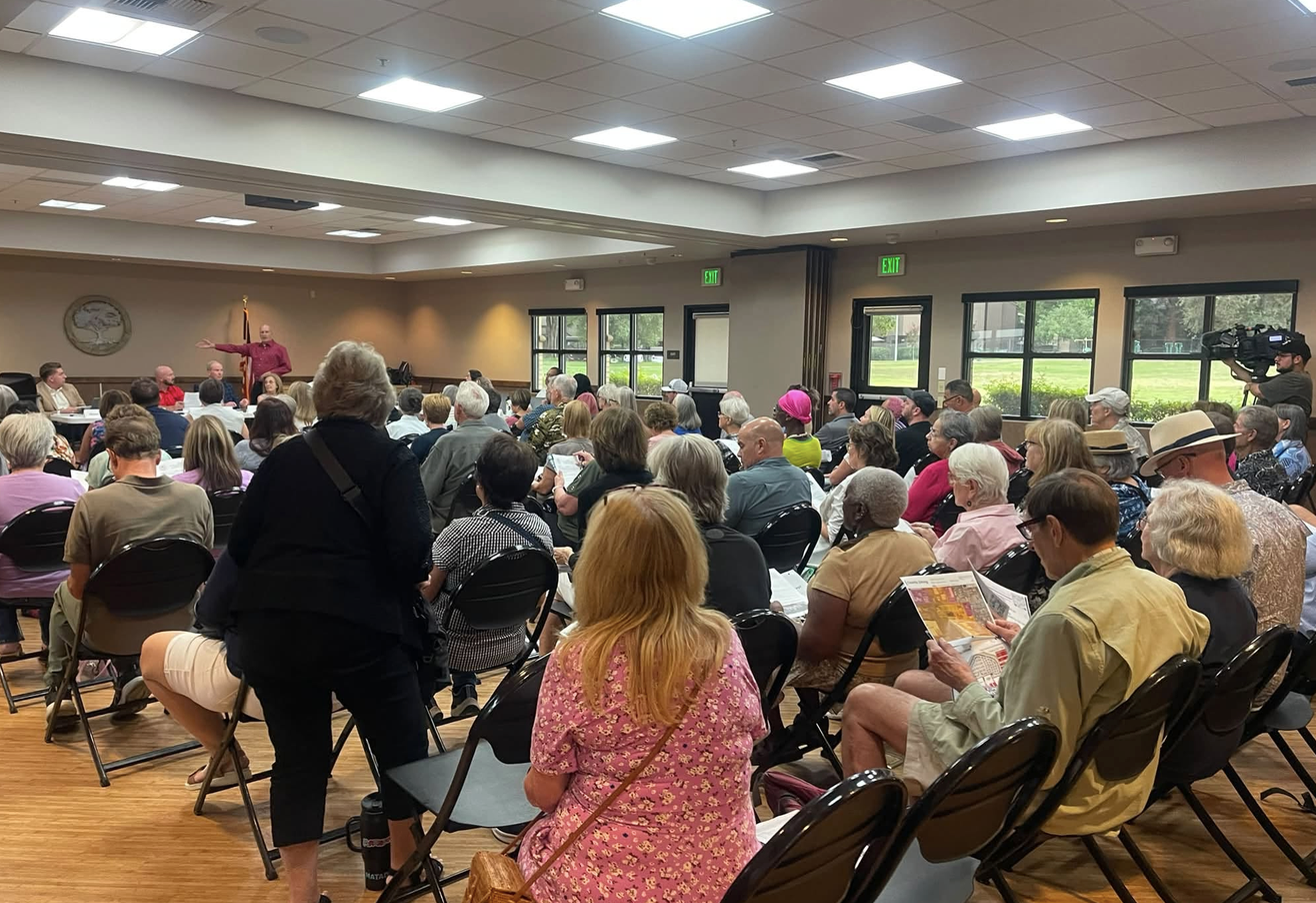 A large group of people is gathered in a meeting space, with a speaker addressing the audience.
