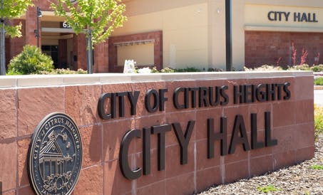 The image shows the exterior of Citrus Heights City Hall, featuring a sign and landscaped area.