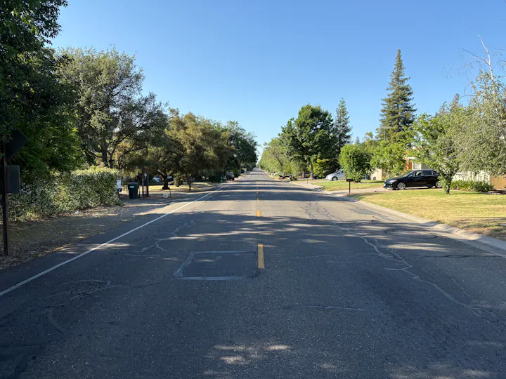 MIssion Avenue, a suburban street with trees lining both sides, parked cars, and a clear blue sky above. It divides Arden Arcvade and Carmichael