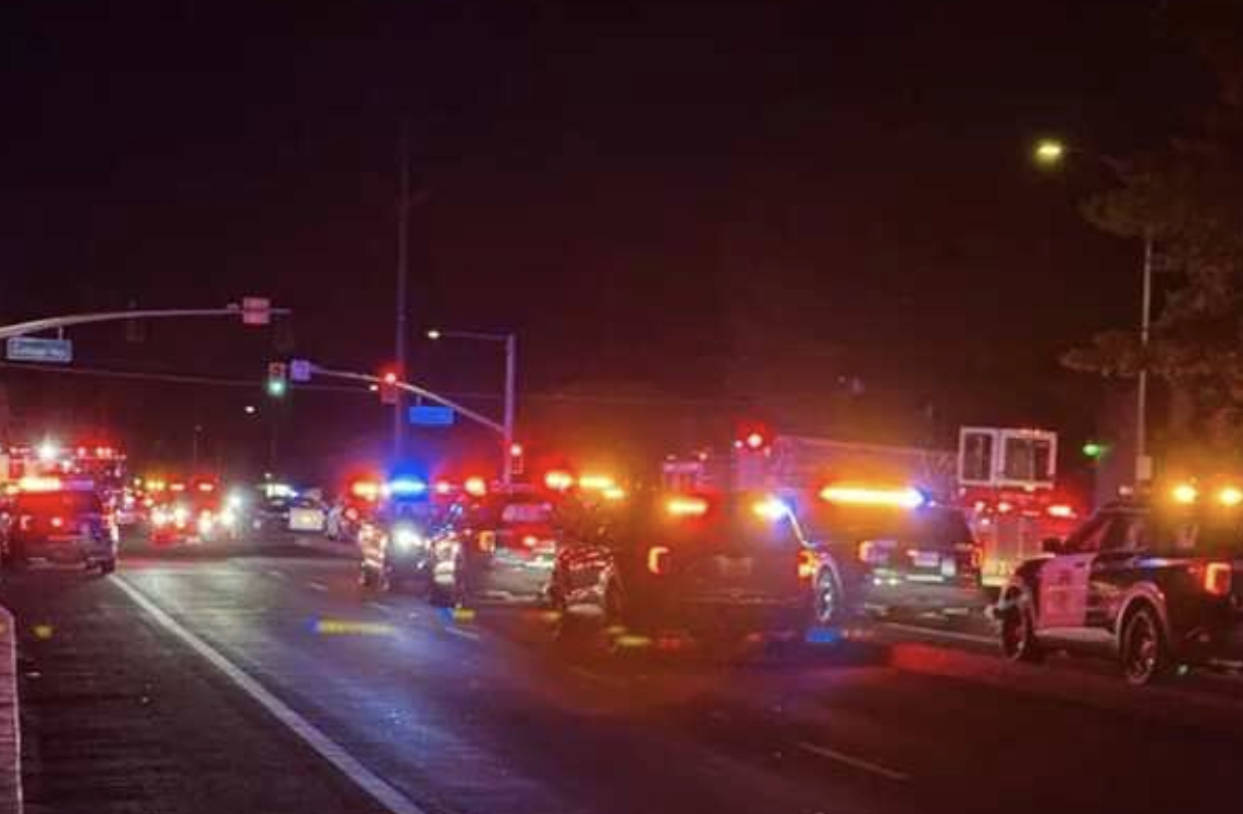 The image shows a nighttime scene with multiple emergency vehicles and flashing lights on a street, indicating an emergency situation.