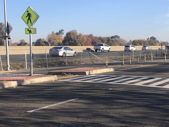 Photo of pedistrian crossing on Auburn Blvd, with broken chain-link fencing that separates Auburn Blvd. from the Business 80 freeway