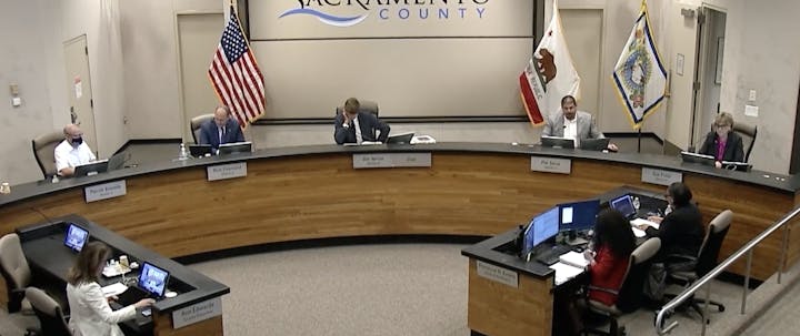A Sacramento County meeting featuring officials seated at a circular table with monitors, discussing local governance.