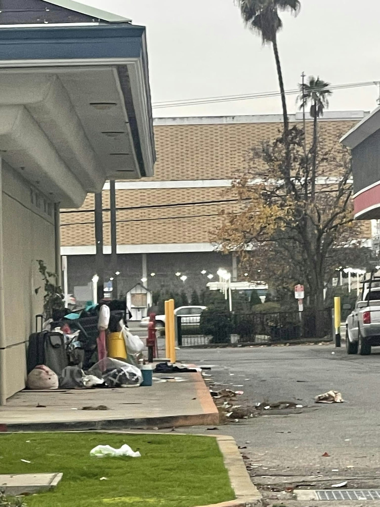 An alleyway with scattered trash, a shopping cart filled with belongings, and parked vehicles.