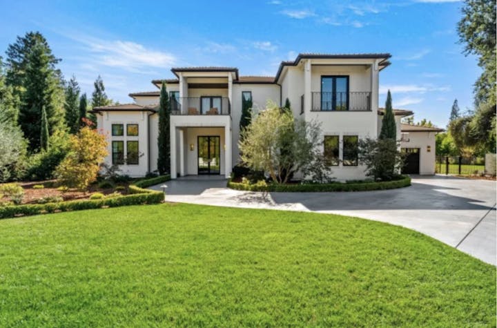 A large, modern two-story house with a landscaped garden and driveway, set against a clear blue sky.