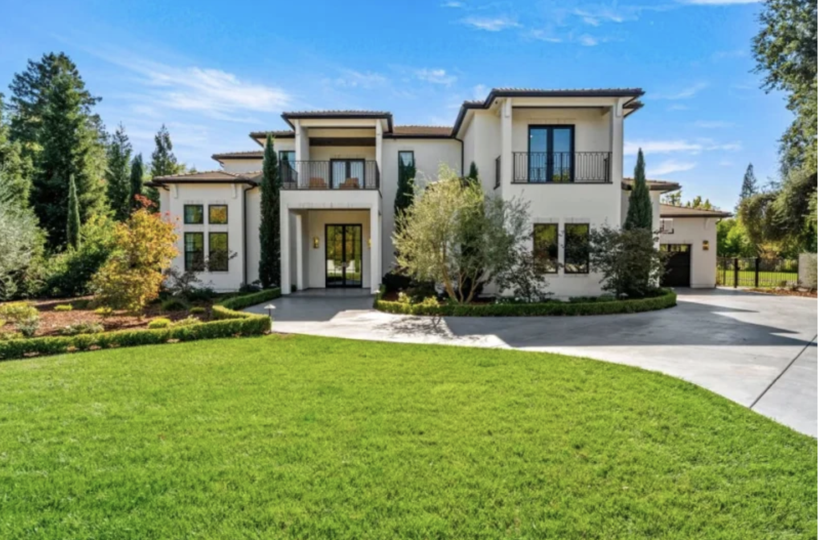 A large, modern two-story house with a landscaped garden and driveway, set against a clear blue sky.