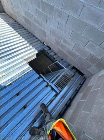 Roof with metal sheets, a person's foot visible, a brick wall, and an open metal hatch.