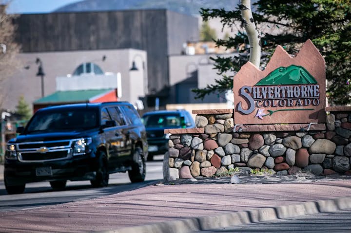 Town sign for Silverthorne, Colorado, with a stone base. Black vehicle in the background.