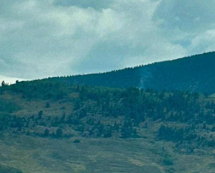 A mountainous landscape with green foliage, rocky terrain, and a hint of smoke rising, under a cloudy sky.