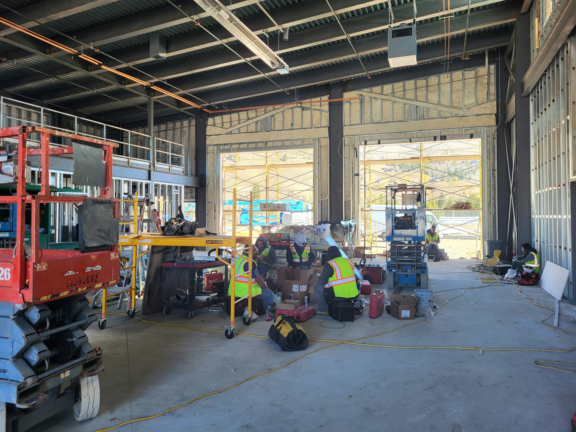 Busy construction site interior with workers, equipment, and scattered building materials.
