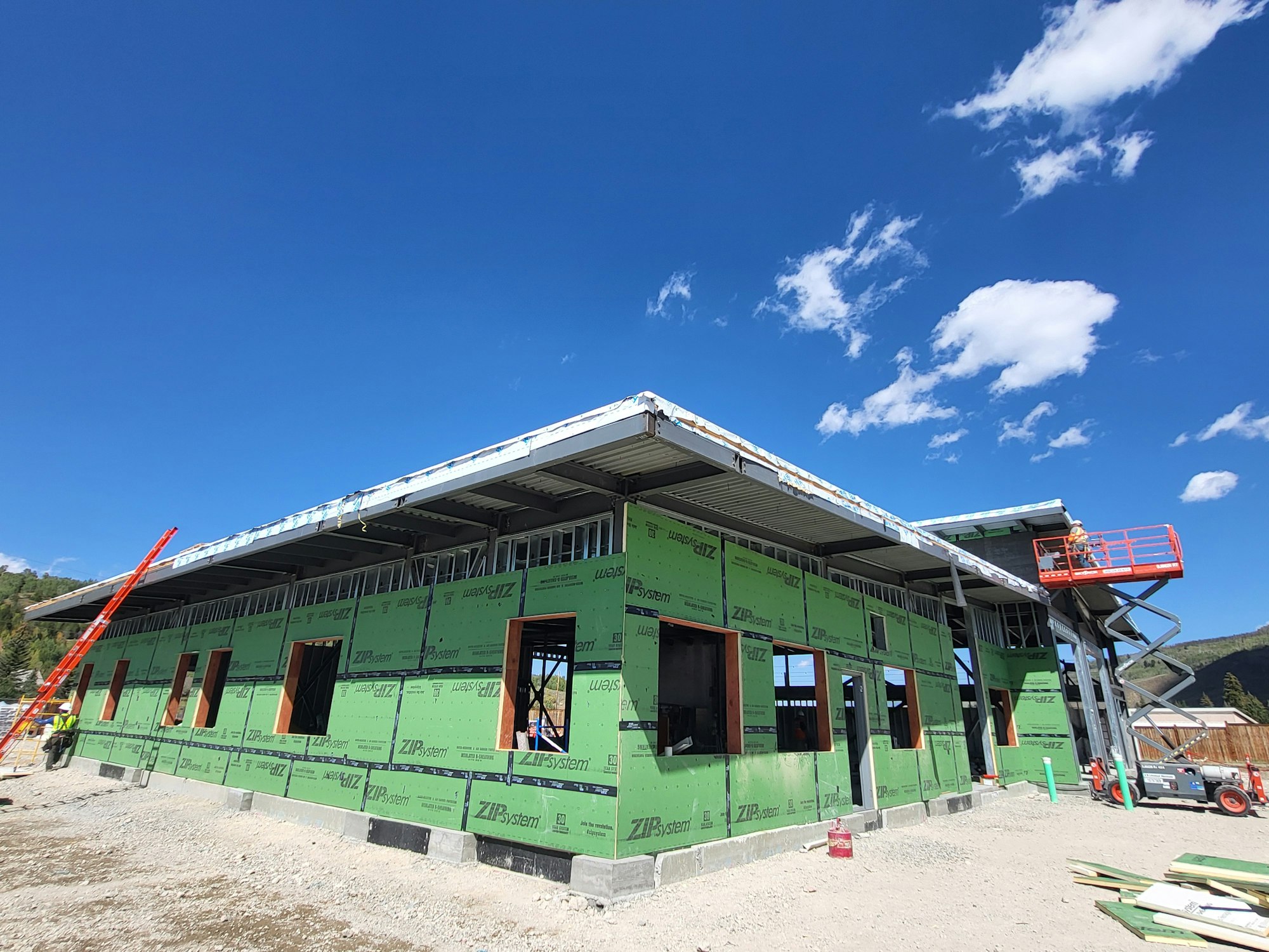 Construction site with unfinished building, workers, and equipment under a blue sky.