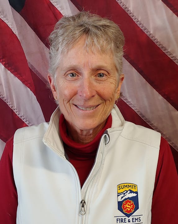 A smiling person with a Summit Fire & EMS patch on their jacket, with an American flag in the background.