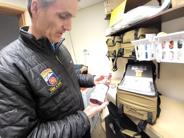 A person in a Summit Fire & EMS jacket examines a medical bag, holding a bottle and surrounded by emergency supplies.