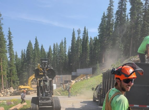 Construction site with workers, machinery, and trees in the background.