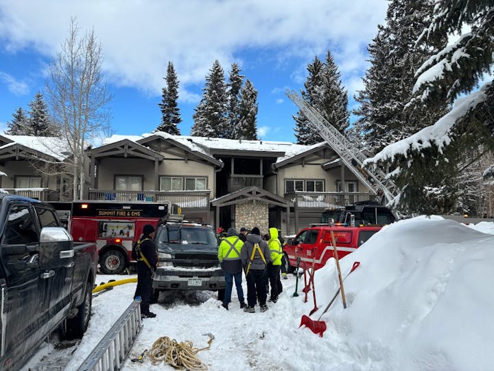 Firefighters in winter gear outside a snow-covered building with fire trucks and equipment.